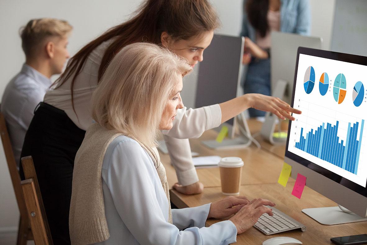 Woman helping someone at a laptop sat at a desk