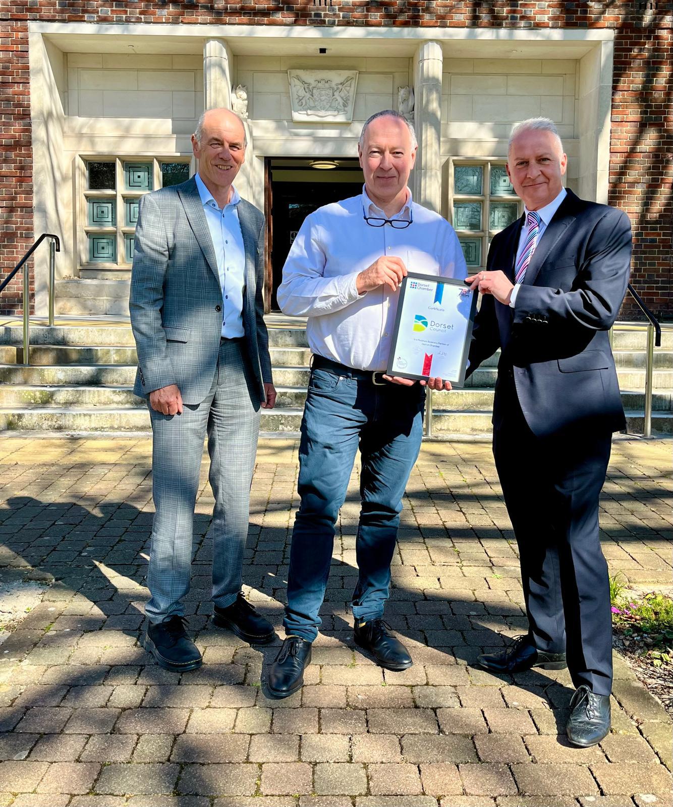 Cllr Richard Biggs, Cllr Nick Ireland and Ian Girling stood in front of County Hall exchanging official certification
