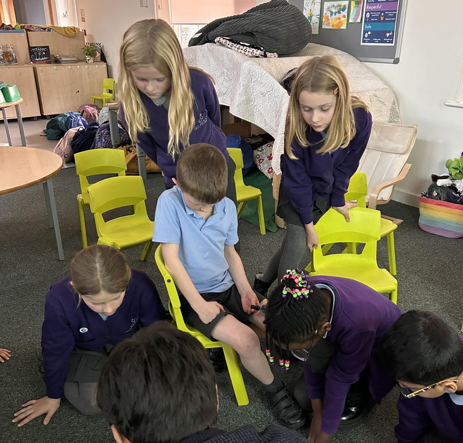 Children wearing blue tops seated on yellow chairs looking at a plan on the floor