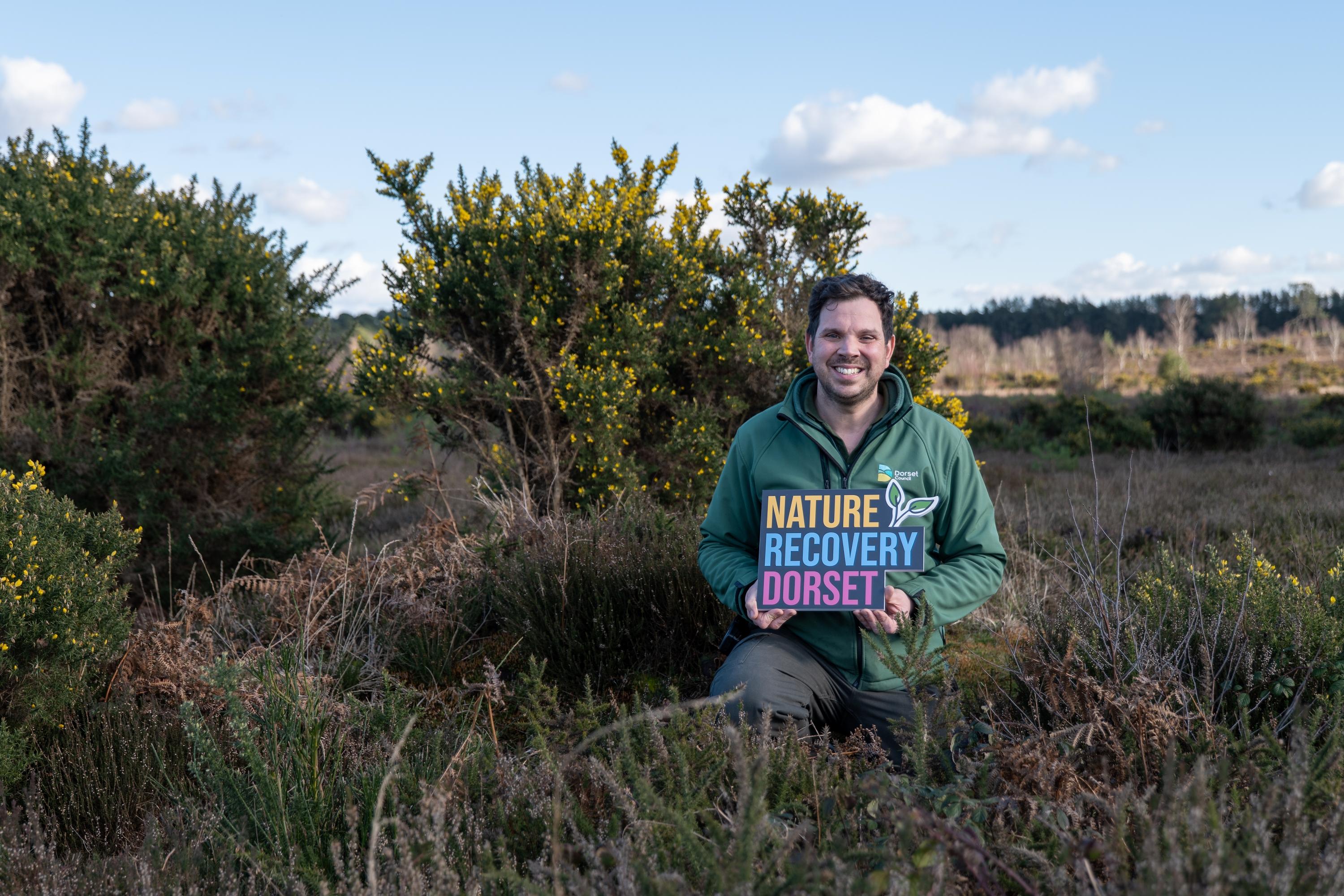 Dorset Council Ranger holding Nature Recovery Dorset sign in a heathland setting