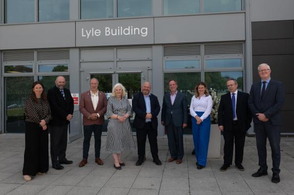 Nine men and women wearing smart clothes standing outside a grey, modern looking building