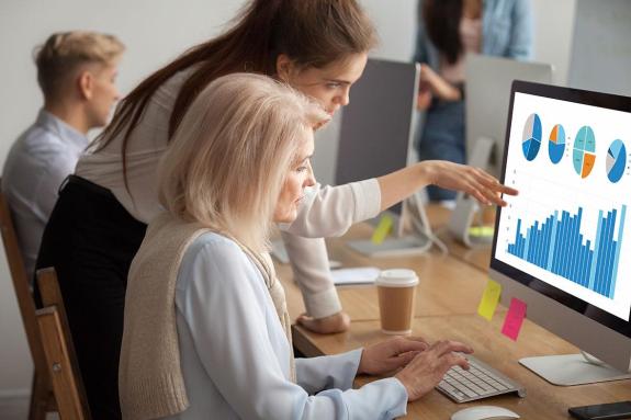 Woman helping someone at a laptop sat at a desk