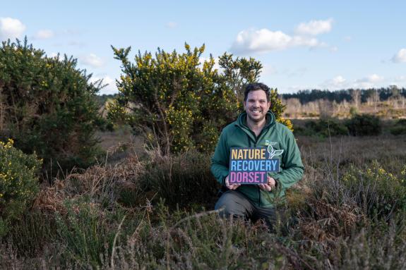 Dorset Council Ranger holding Nature Recovery Dorset sign in a heathland setting