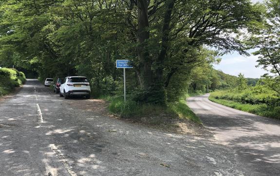 A turning of a main road with a white car, a black car and a silver car parked on the right