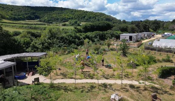 People working on a garden area in the country side, there are outbuildings and a path and it is a hot sunny day